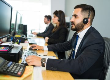 Attractive latin executive offering customer service with a headset and offering tech support at a busy call center